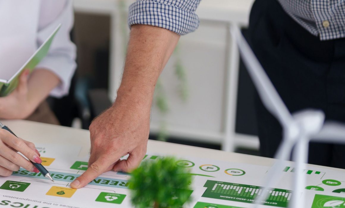 Personas revisando materiales de formación sobre sostenibilidad y medioambiente en una mesa de trabajo, con gráficos de economía verde y energía renovable.