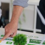 Personas revisando materiales de formación sobre sostenibilidad y medioambiente en una mesa de trabajo, con gráficos de economía verde y energía renovable.